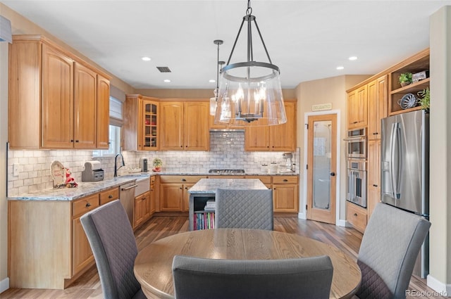 kitchen featuring decorative light fixtures, a center island, light hardwood / wood-style flooring, appliances with stainless steel finishes, and light stone countertops