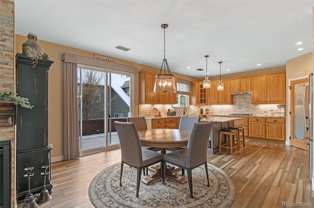 dining area with a healthy amount of sunlight, a stone fireplace, and light hardwood / wood-style flooring