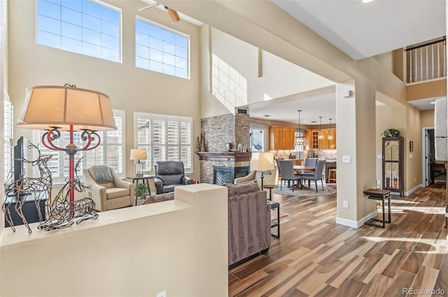 living room with a high ceiling, wood-type flooring, and a stone fireplace