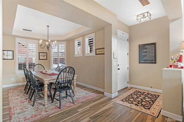 dining area with hardwood / wood-style flooring, a raised ceiling, and an inviting chandelier