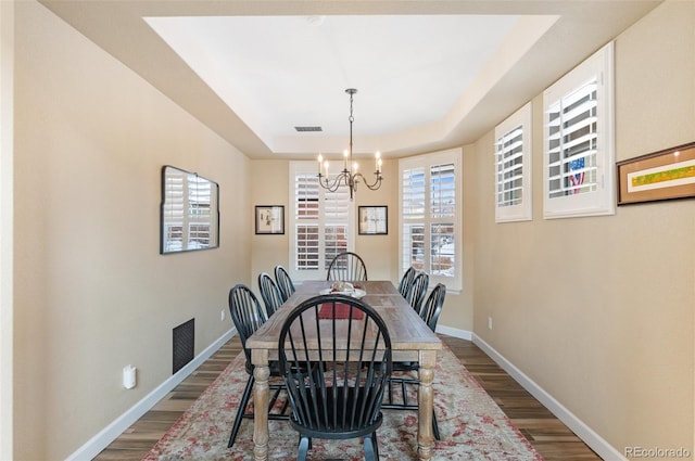 dining space with hardwood / wood-style flooring, a chandelier, and a tray ceiling