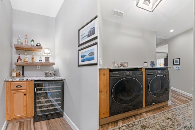 laundry area featuring light wood-type flooring, bar, wine cooler, and independent washer and dryer