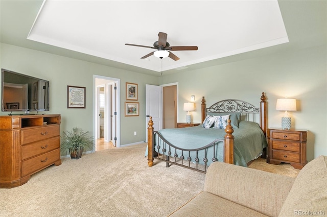 bedroom with ceiling fan, connected bathroom, a tray ceiling, and light carpet