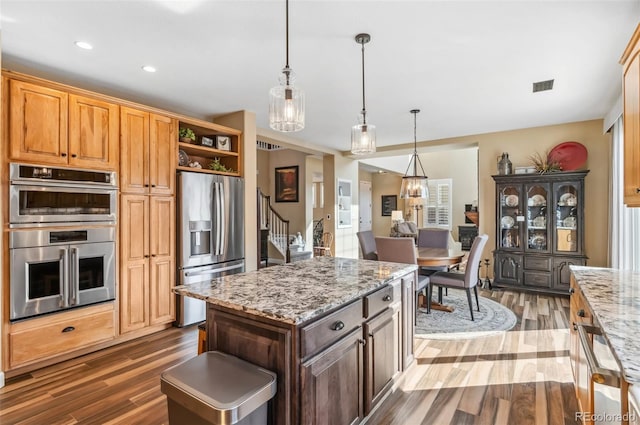 kitchen featuring hanging light fixtures, light stone countertops, appliances with stainless steel finishes, and dark wood-type flooring