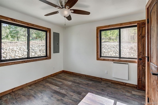 empty room featuring dark wood-style flooring, plenty of natural light, electric panel, and radiator