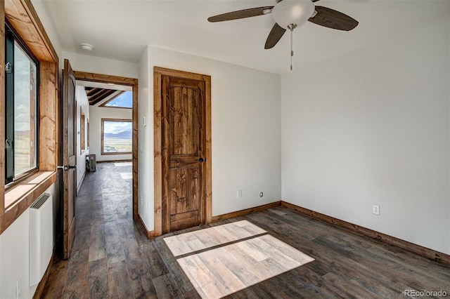 empty room with dark wood-style floors, baseboards, and radiator heating unit