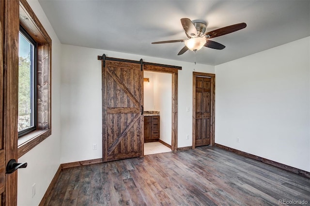 unfurnished bedroom with a barn door, baseboards, connected bathroom, ceiling fan, and wood finished floors