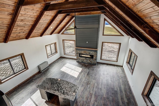 unfurnished living room with beam ceiling, a stone fireplace, wood finished floors, wooden ceiling, and baseboards