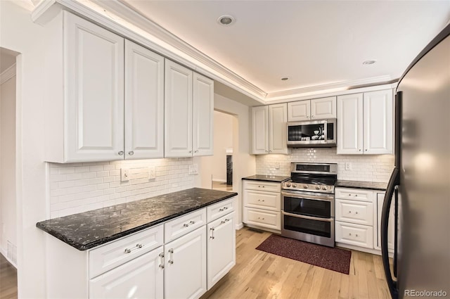 kitchen with white cabinetry, backsplash, stainless steel appliances, dark stone counters, and light wood-type flooring