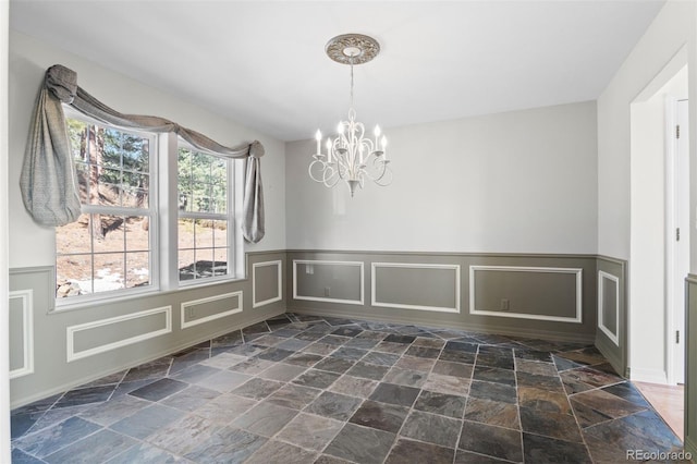 6904 Sprucedale Park Way, Evergreen, CO 80439 - unfurnished dining area featuring a chandelier, stone tile flooring, a decorative wall, and a wainscoted wall