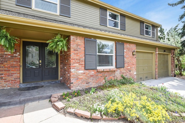 entrance to property with brick siding, a garage, concrete driveway, and french doors