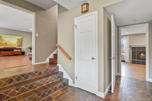 stairway featuring stone tile flooring, a textured wall, a tiled fireplace, and baseboards
