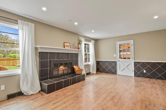 living area featuring healthy amount of natural light, wood finished floors, a tile fireplace, recessed lighting, and a wainscoted wall