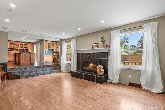 living area with wood finished floors, a tile fireplace, and recessed lighting