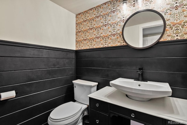 bathroom featuring wallpapered walls, wainscoting, toilet, and vanity