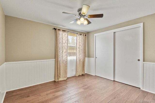 unfurnished bedroom featuring wainscoting, hardwood / wood-style floors, a closet, and ceiling fan