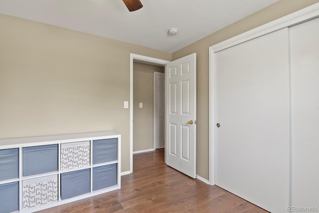 unfurnished bedroom with dark wood-style flooring, a closet, baseboards, and ceiling fan