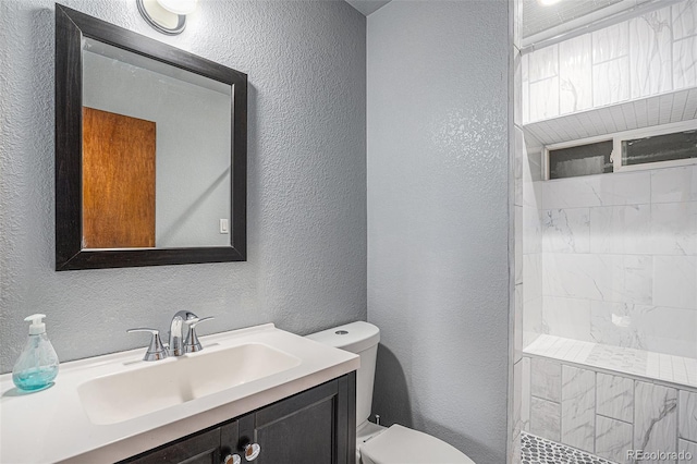 full bathroom featuring a tile shower, toilet, vanity, and a textured wall