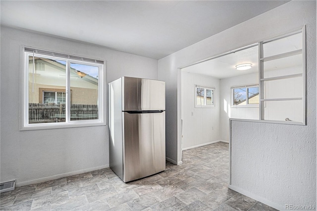kitchen featuring stone finish floor, baseboards, visible vents, and freestanding refrigerator