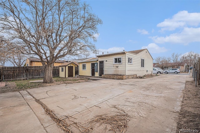 back of house with an outbuilding, a storage shed, concrete driveway, and fence