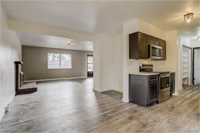 kitchen with a brick fireplace, light hardwood / wood-style flooring, dark brown cabinets, and appliances with stainless steel finishes