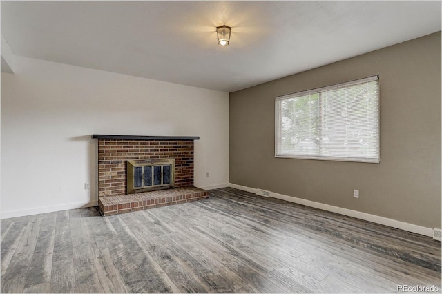 unfurnished living room featuring wood-type flooring and a brick fireplace