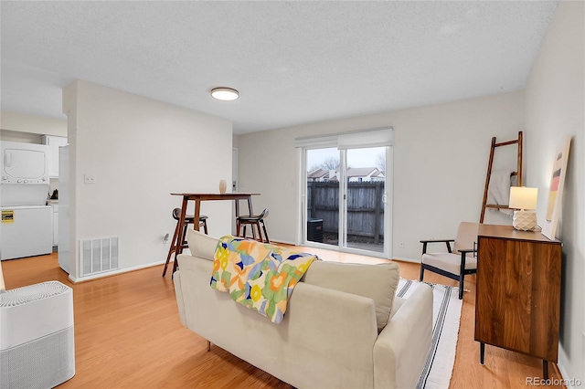 living area with stacked washer / drying machine, baseboards, visible vents, and light wood-style floors