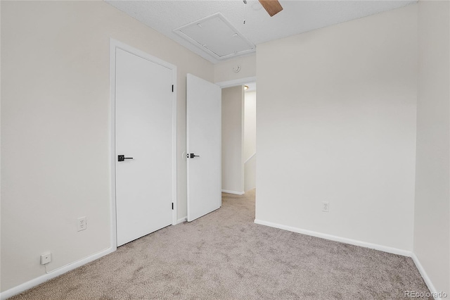unfurnished bedroom featuring baseboards, a ceiling fan, attic access, and carpet