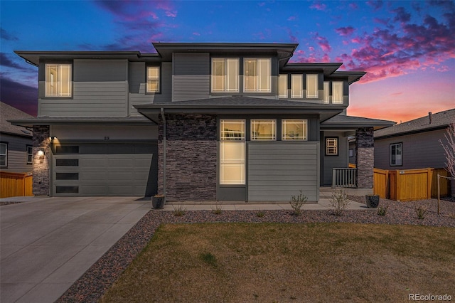 prairie-style house featuring concrete driveway, a garage, stone siding, and a front lawn