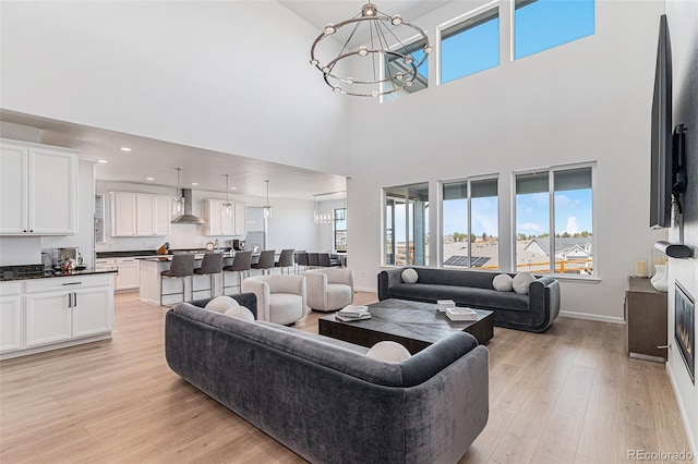 living room with light wood-style flooring, a notable chandelier, baseboards, and a towering ceiling