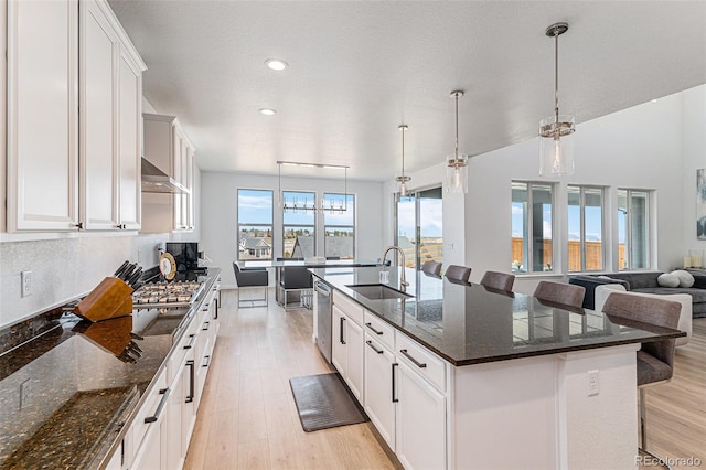 kitchen featuring a sink, a kitchen island with sink, a kitchen bar, light wood-style floors, and stainless steel dishwasher