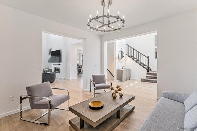 living area with light wood-style flooring, stairway, an inviting chandelier, and baseboards