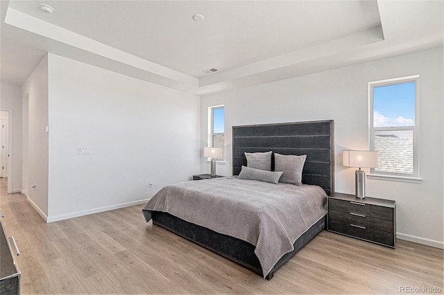 bedroom featuring baseboards, a raised ceiling, and light wood finished floors