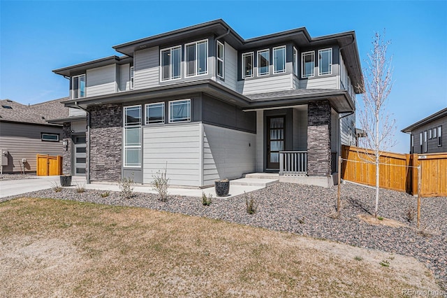 prairie-style home featuring stone siding and fence