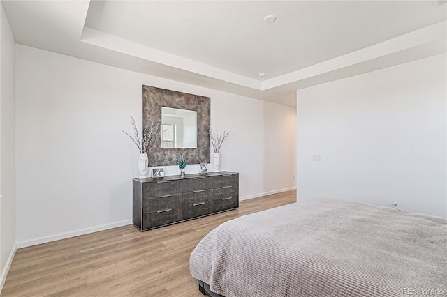 bedroom featuring light wood finished floors, baseboards, and a raised ceiling
