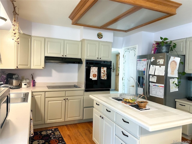 kitchen with tile counters, cooktop, stainless steel fridge with ice dispenser, oven, and a kitchen island