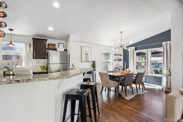 kitchen featuring light stone countertops, appliances with stainless steel finishes, pendant lighting, dark wood-type flooring, and a breakfast bar area