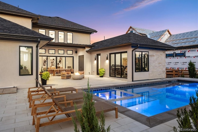 back of property at dusk featuring a patio, a pool with connected hot tub, an outdoor living space, and stucco siding