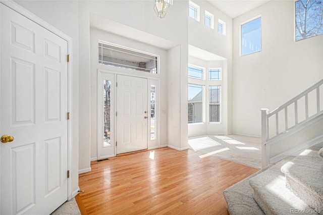 entrance foyer with stairway, a healthy amount of sunlight, light wood-type flooring, and a towering ceiling