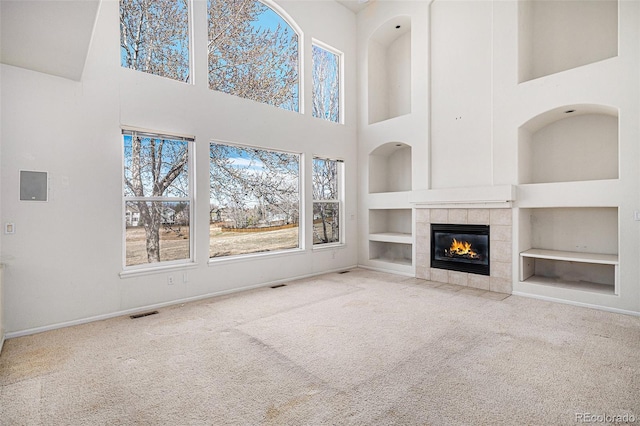 unfurnished living room featuring a tiled fireplace, built in shelves, carpet, and plenty of natural light