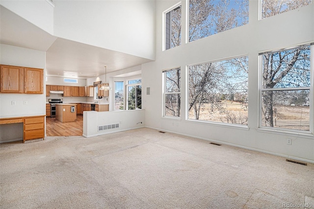 unfurnished living room featuring light colored carpet, visible vents, a towering ceiling, and baseboards