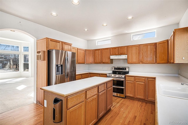 kitchen with a kitchen island, a sink, light countertops, under cabinet range hood, and appliances with stainless steel finishes