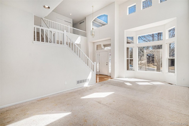 carpeted entrance foyer with visible vents, baseboards, stairway, recessed lighting, and a towering ceiling