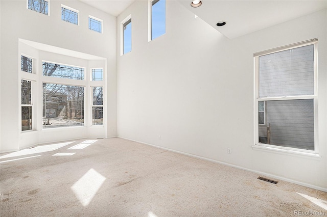 unfurnished room featuring visible vents, baseboards, carpet, and a towering ceiling