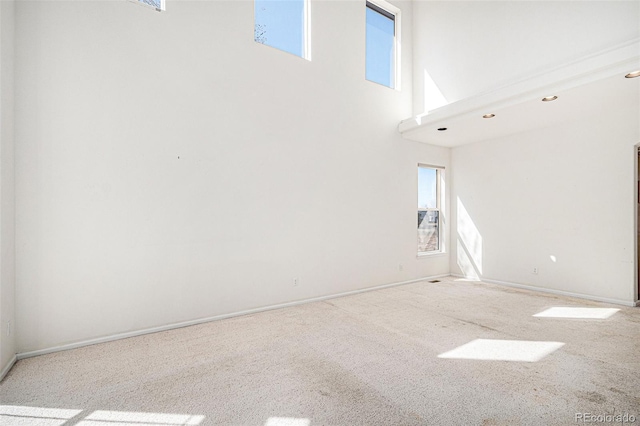 carpeted empty room with a high ceiling and baseboards