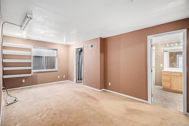 spare room with a textured ceiling, baseboards, visible vents, and light carpet