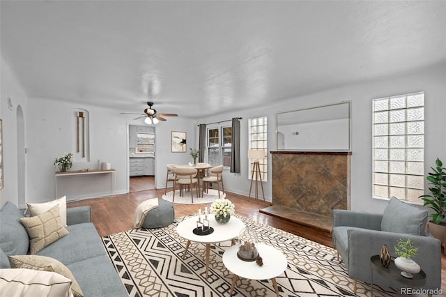 living room with arched walkways, wood finished floors, a ceiling fan, and baseboards