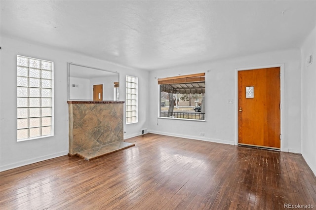 unfurnished living room with plenty of natural light, wood finished floors, visible vents, and baseboards