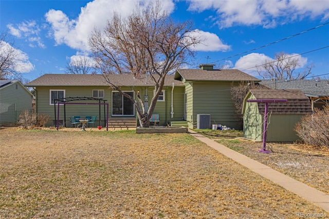 back of property featuring entry steps, a storage shed, a lawn, an outdoor structure, and central air condition unit