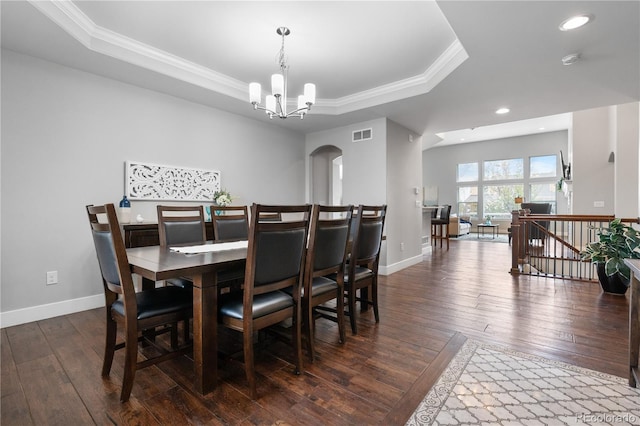 dining space featuring dark wood-style flooring, a notable chandelier, a tray ceiling, and crown molding